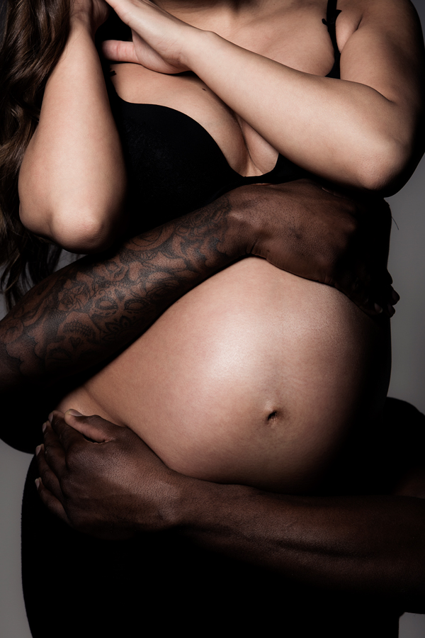 zwangerschap shoot getatoeëerde armen om buik van vrouw met zwarte lingerie